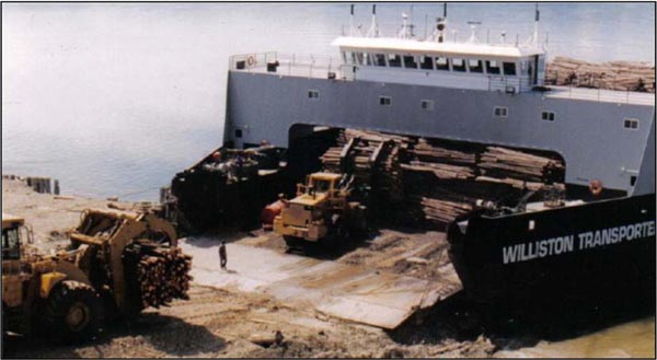 The MV Williston Transporter barge being loaded with logs at the shoreline.